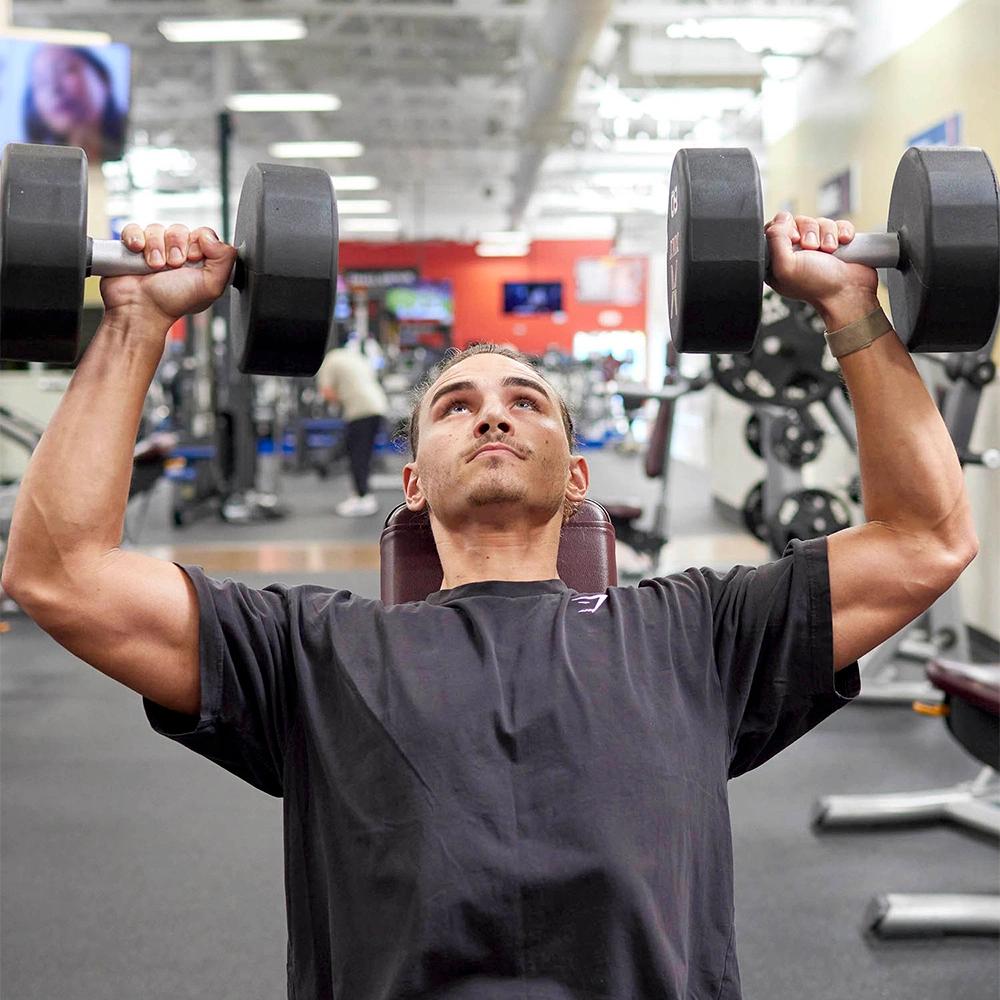 Man performing overhead press with two dumbbells